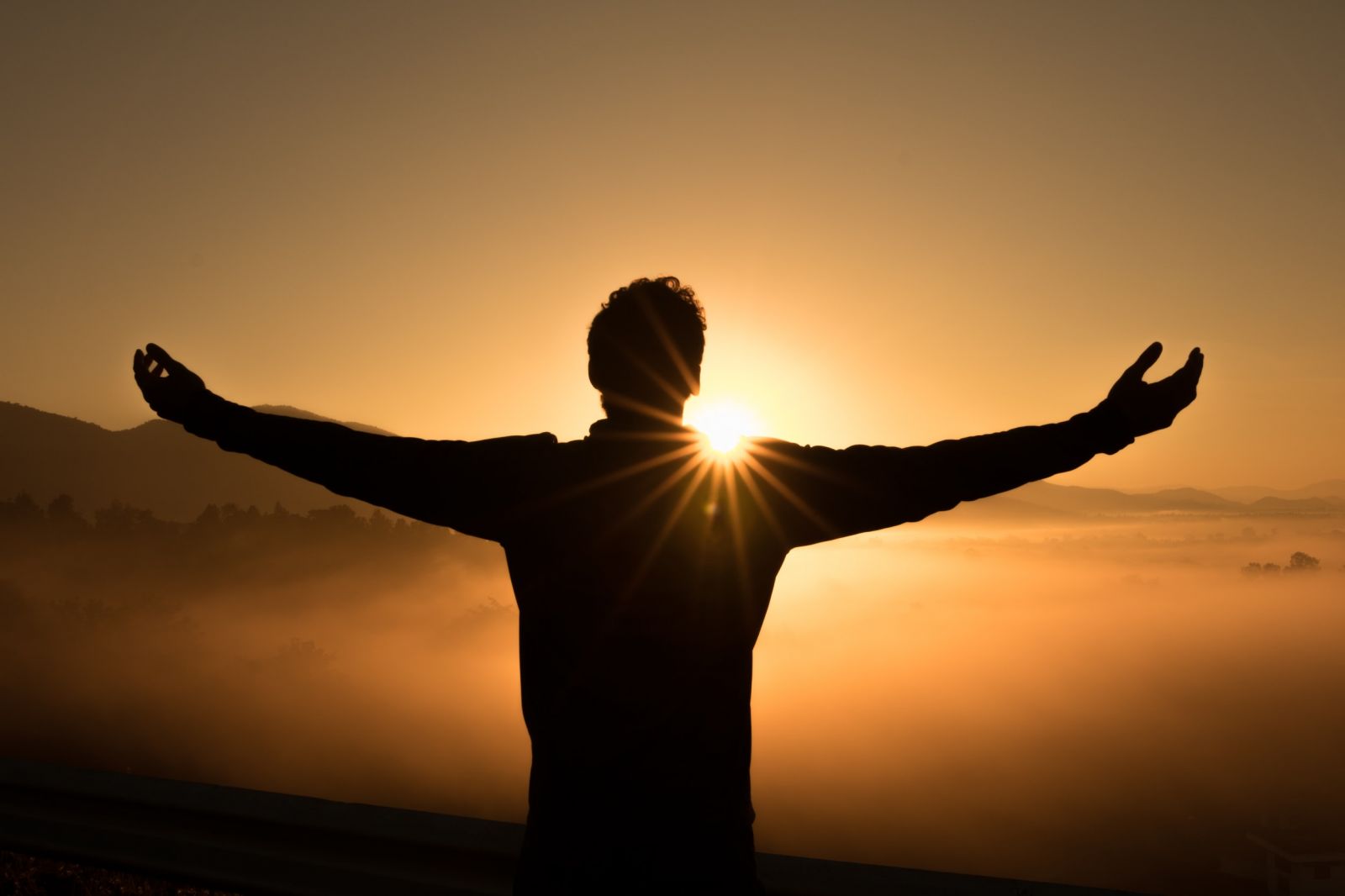 man with arms outstretched at sunrise